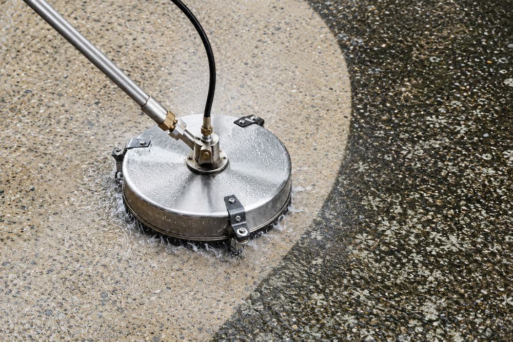 Rotary surface cleaner lifting black mould off a concrete driveway